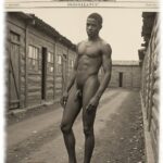 Vintage-Poster, Young Buck, dunkelhäutiger Mann zwischen Elendshütten stehend, nackt. wohlgeformter Funke des Eros.