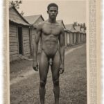 Vintage-Poster, Young Buck, dunkelhäutige Mann vor Elendshütten stehend, nackt.