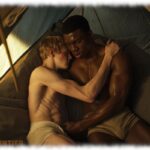 Zwei Twinks umarmen sich im Zelt liegend, Hand an der leichte Auswölbung des anderen,
