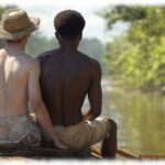 Zwei Twinks sitzen im Boot, Hand des einen unter dem Po des anderen.