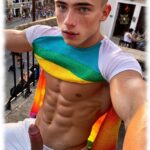 Blonder Twink beim Straßen-Karneval sitzend, fremde Hand umfasst seine Granitsäule der Lust.