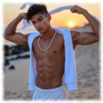 Twink am Strand stehend. Hände über dem Kopf, freier Oberkörper.