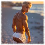 Blonder Twink am Strand stehend. Short bedeckt nur den halben Po.