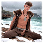 Odin´s Sohn mit Fellweste sitzt breitbeinig am Strand, geöffnete Hose gibt den Herold der Sehnsucht frei.