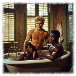 Zwei dunkelhäutige Männer in Badewanne, blonder Mann legt sein Lustpendel auf eine Schulter.