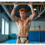 Rothaariger Twink in Sporthalle am Reck, Shorts mit leichter Auswölbung.