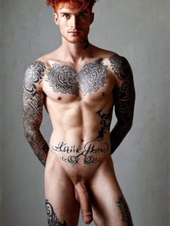 rothaariger, tätowierter Mann vor grauem Hintergrund stehend